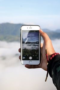 Man photographing with mobile phone against sky