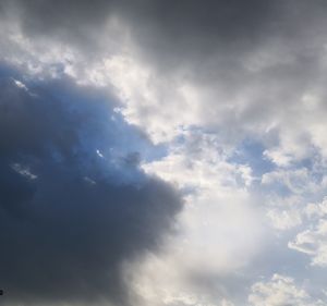 Low angle view of sunlight streaming through clouds