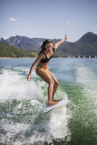 Woman surfing in lake against mountain range