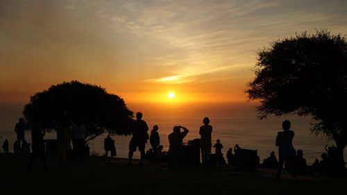 Silhouette people by sea against sky during sunset