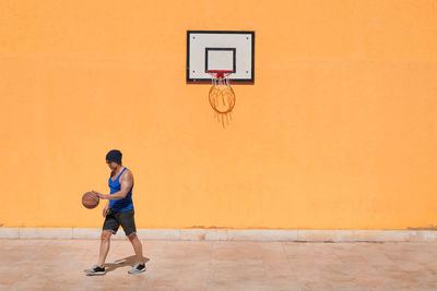 Man playing basketball against orange wall during sunny day 