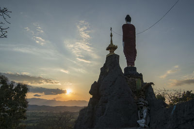 Low angle view of statue by building against sky during sunset