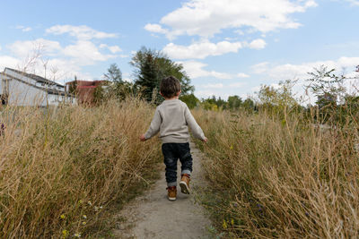 Rear view of boy on dirt road against sky