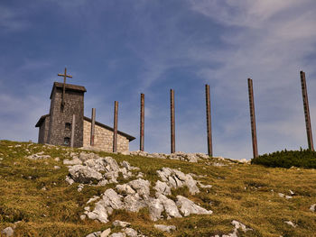 Cross on rock by building against sky