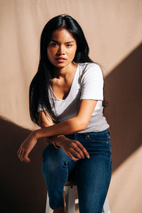 Portrait of beautiful young woman sitting against wall