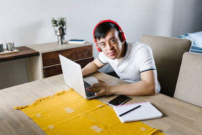 High angle of content latin teen boy with down syndrome browsing netbook while sitting at table and studying online from home