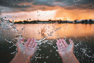 Cropped hands of person splashing water during sunset