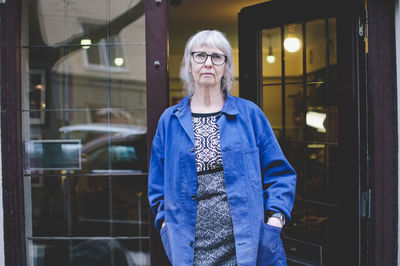 Portrait of senior female owner standing with hands in pockets outside jewelry store