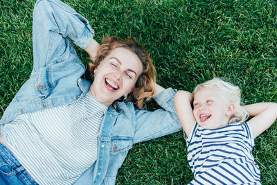 Top view of carefree laughing mother and daughter lying on green grass and enjoying summer