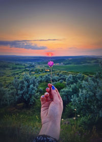 Cropped hand of person holding hot air balloons against sky during sunset