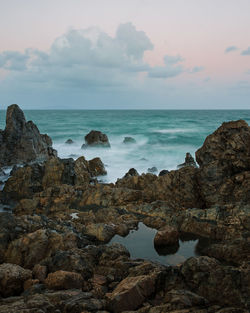 Scenic view of sea with rocky shore against sky during sunset