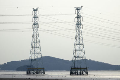 Electricity pylons at beach against clear sky