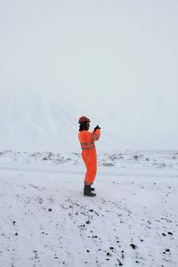 Side view of man wearing protective workwear standing on snow against clear sky
