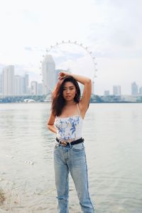 Fashionable young woman standing against sea and urban skyline