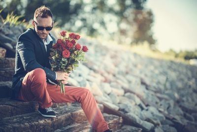 Man holding rose bouquet while sitting on staircase