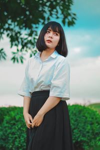 Beautiful young woman standing on field against sky