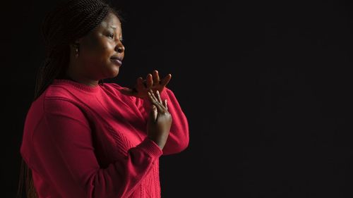 Side view of young woman standing against black background