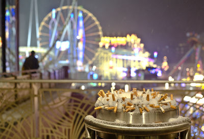 Close-up of cigarette butts on snow covered garbage can in city at night