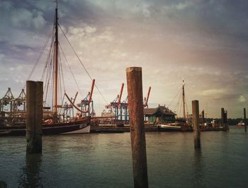 Wooden posts and boats on river against cloudy sky