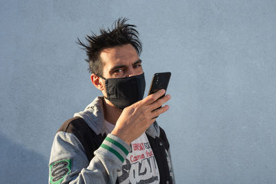 Portrait of young man using mobile phone against wall