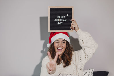 Portrait of woman winking and gesturing with merry christmas text at home