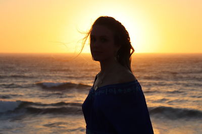 Woman standing at beach against sky during sunset