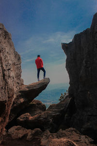 Man standing on rock formation against sky