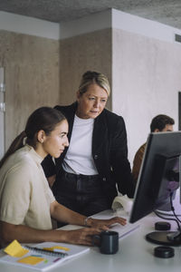 Female professor explaining phd student over computer at desk in innovation lab