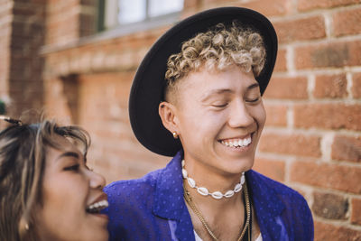 Happy young man wearing hat by female friend laughing against building