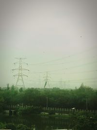 Electricity pylon by trees against sky