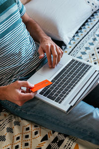 Close up hand holding credit card and shopping online on bed.