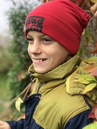 A boy in a pink hat stands on a background red autumn leaves of wild grapes and a smile