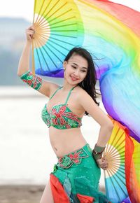 Smiling young woman holding colorful hand fans at beach