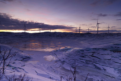 Snow covered landscape against sky during sunset