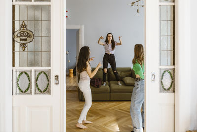 Smiling young female friends dancing in living room seen through doorway