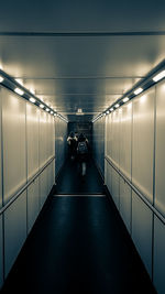 Rear view of people walking on illuminated corridor