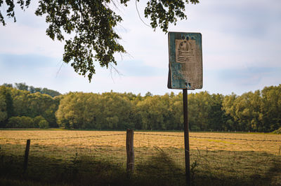 Information sign on wooden post on field against sky