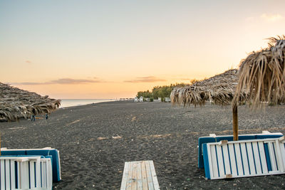 Chairs on beach against sky during sunset