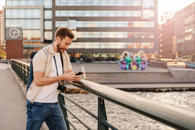 Mid adult man using smart phone while standing by railing in city