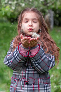 Girl blowing on a dandelion in a spring park. happy child has fun outdoors.