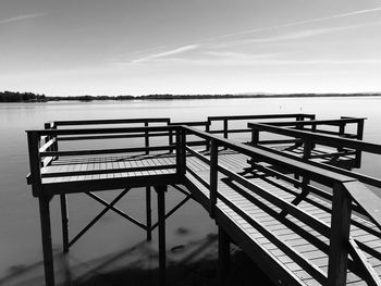 Empty bench on pier by lake against sky