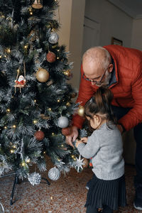 Grandparents decorate the christmas tree with their little granddaughter