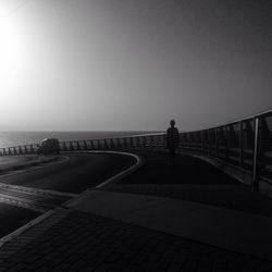 Woman standing on railing by sea against clear sky