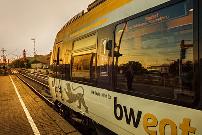 Train on railroad station platform against sky at sunset
