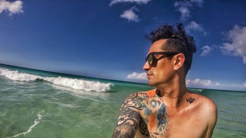 Close-up of shirtless man wearing sunglasses in sea against blue sky