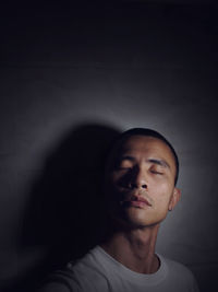 Close-up of sad man standing with eyes closed against wall in darkroom