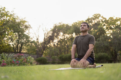 Portrait of young man sitting on grass against trees