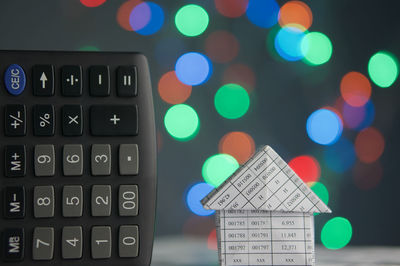 Close-up of calculator and model house against defocused multi colored lights