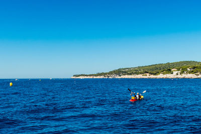 Rear view of people enjoying in boat on sea against clear blue sky