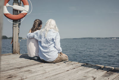 Mother and daughter looking at the sea, sitting on jetty, rear view